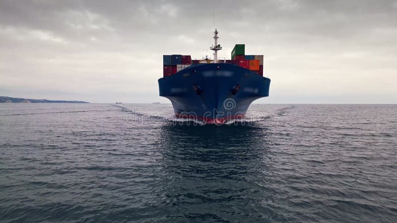 Front view of a blue container ship sailing through calm waters under a cloudy sky, heading towards the port stock footage