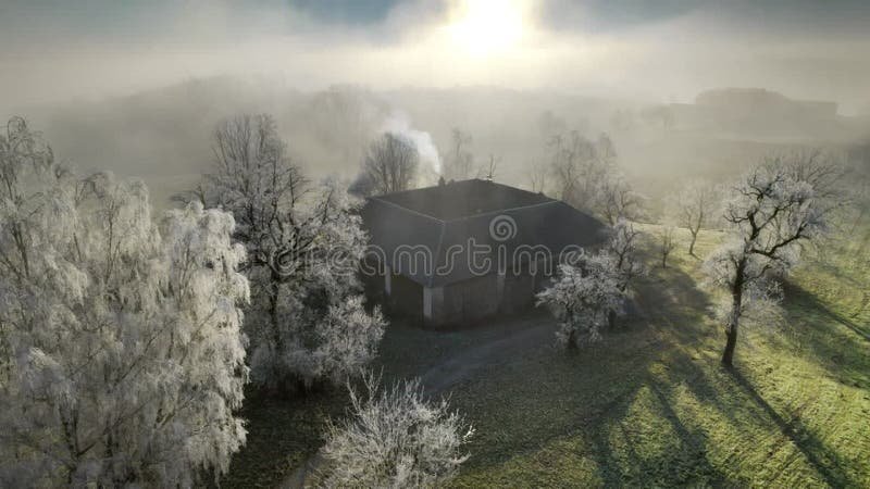 Old farmhouse in winter hoarfrost landscape. Old farmhouse in winter hoarfrost, with the sun shining through mist and trees, aerial footage stock video footage