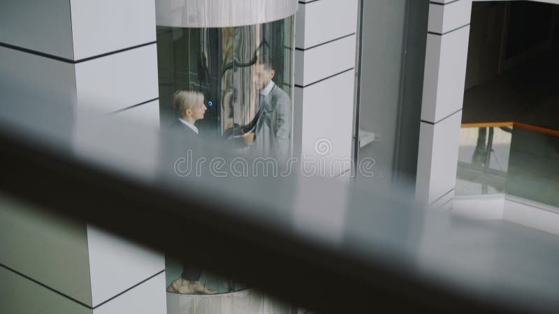 Tilt up of businesswoman and businessman colleagues talking in moving elevator and come out from it in modern business stock video
